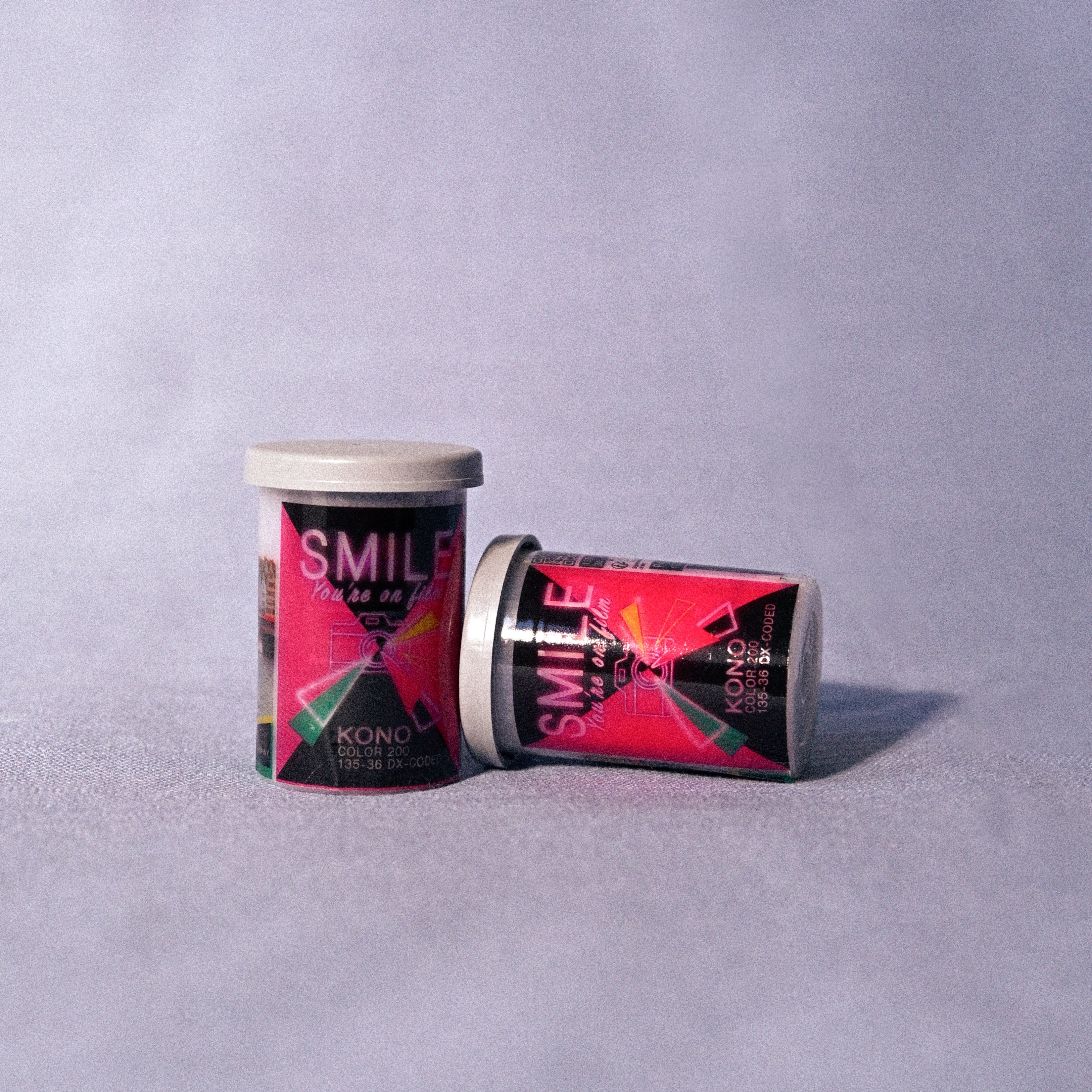 Two cannisters of Kono Smile 200 35mm film on a gray background