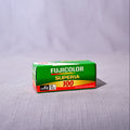 A vintage box of Fujicolor Superia 100 film placed on a light gray textured fabric surface with a matching fabric backdrop.