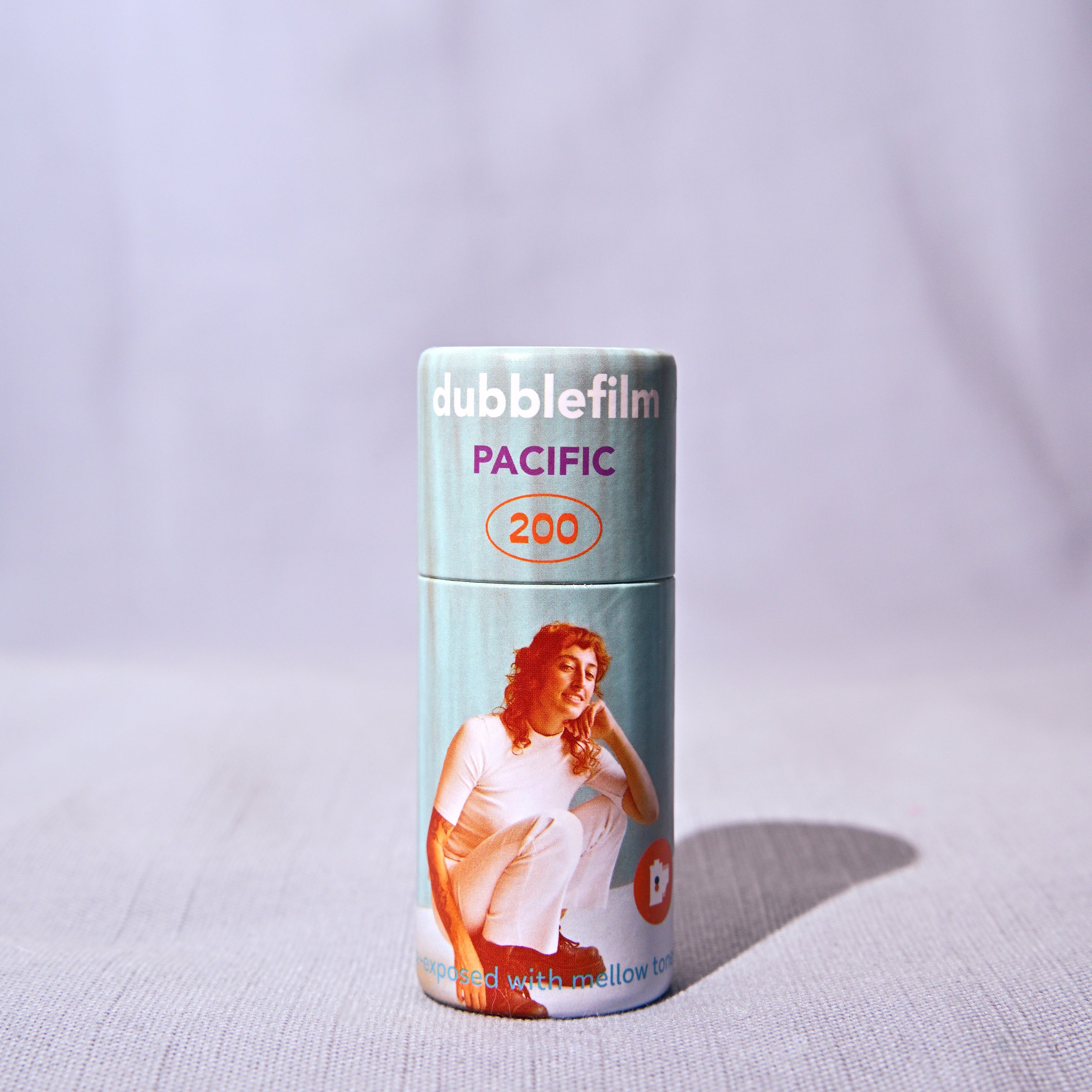A single roll of bubblefilm photographic negative film, labeled 'PACIFIC 200', standing upright on a light gray textured fabric surface with a soft shadow cast to the right.