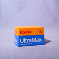 A box of Kodak UltraMax color negative film, 135mm 400, positioned on a textured light gray fabric surface with a matching fabric backdrop.