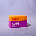 A box of Kodak Gold Color Negative Film, 35mm, standing upright on a textured light gray surface with a draped fabric backdrop.
