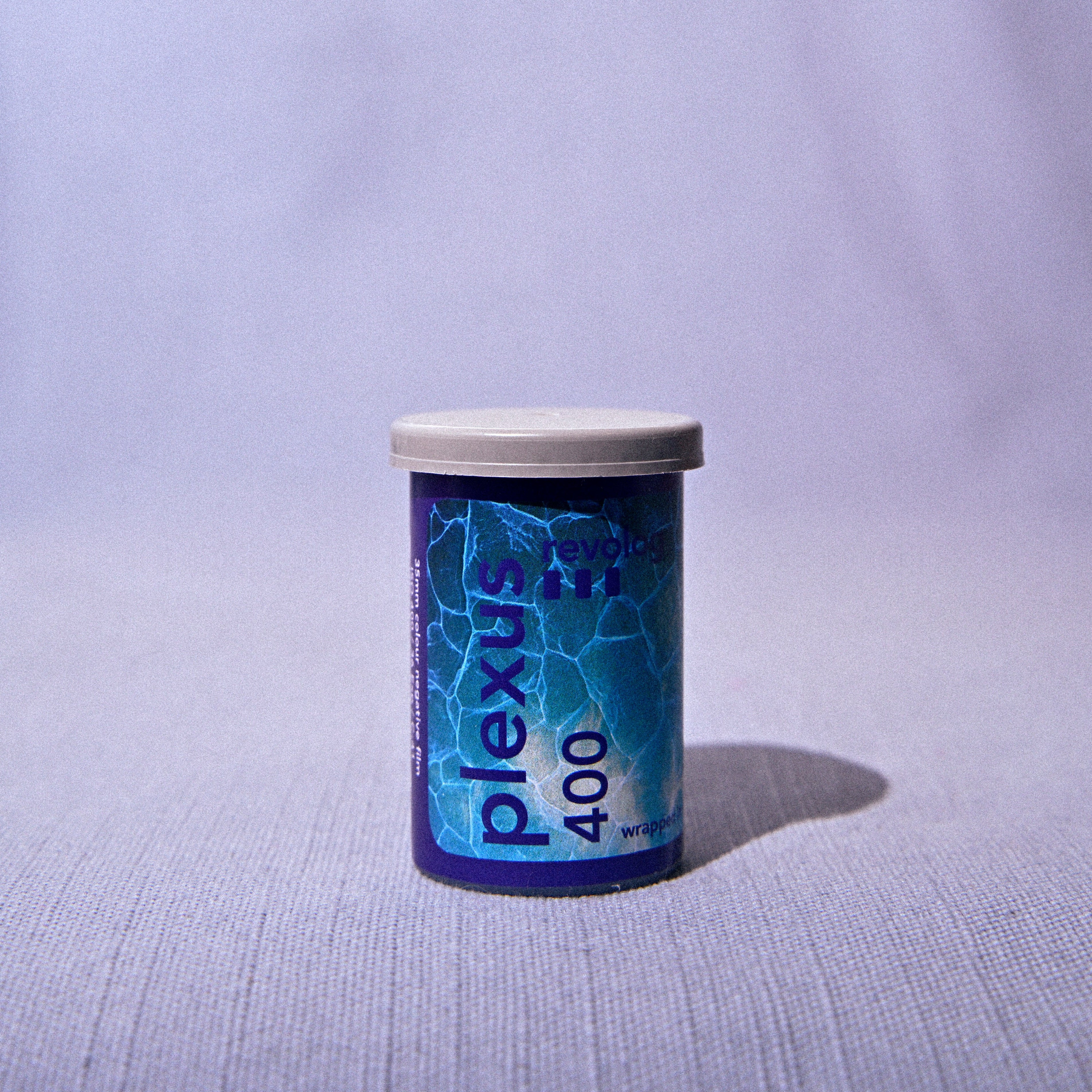 A single canister of Plexus 400 film positioned on a light gray textured surface against a matching light gray fabric backdrop.