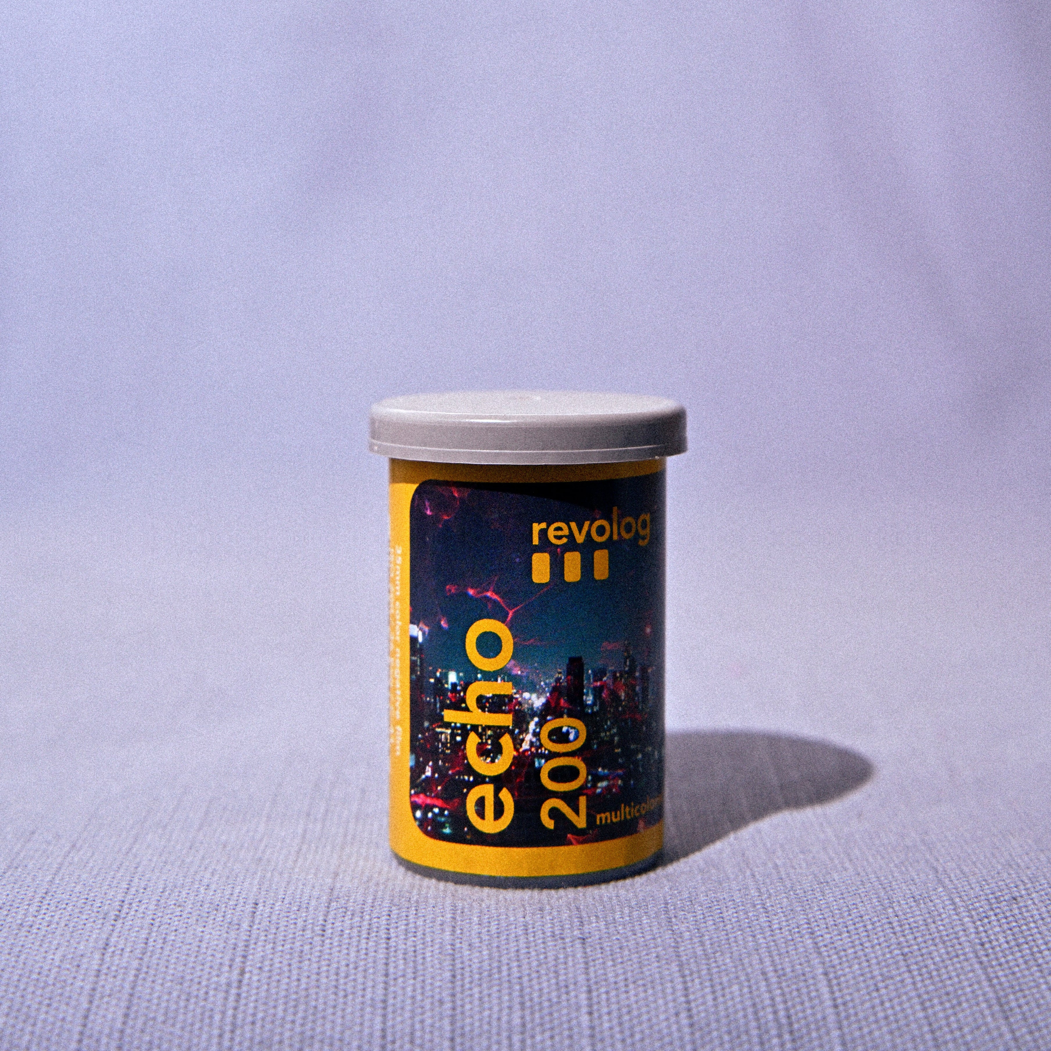 A small cylindrical container labeled 'revolution echo 200' with a yellow and dark label and a light gray lid, standing on a light gray fabric surface with a soft shadow.