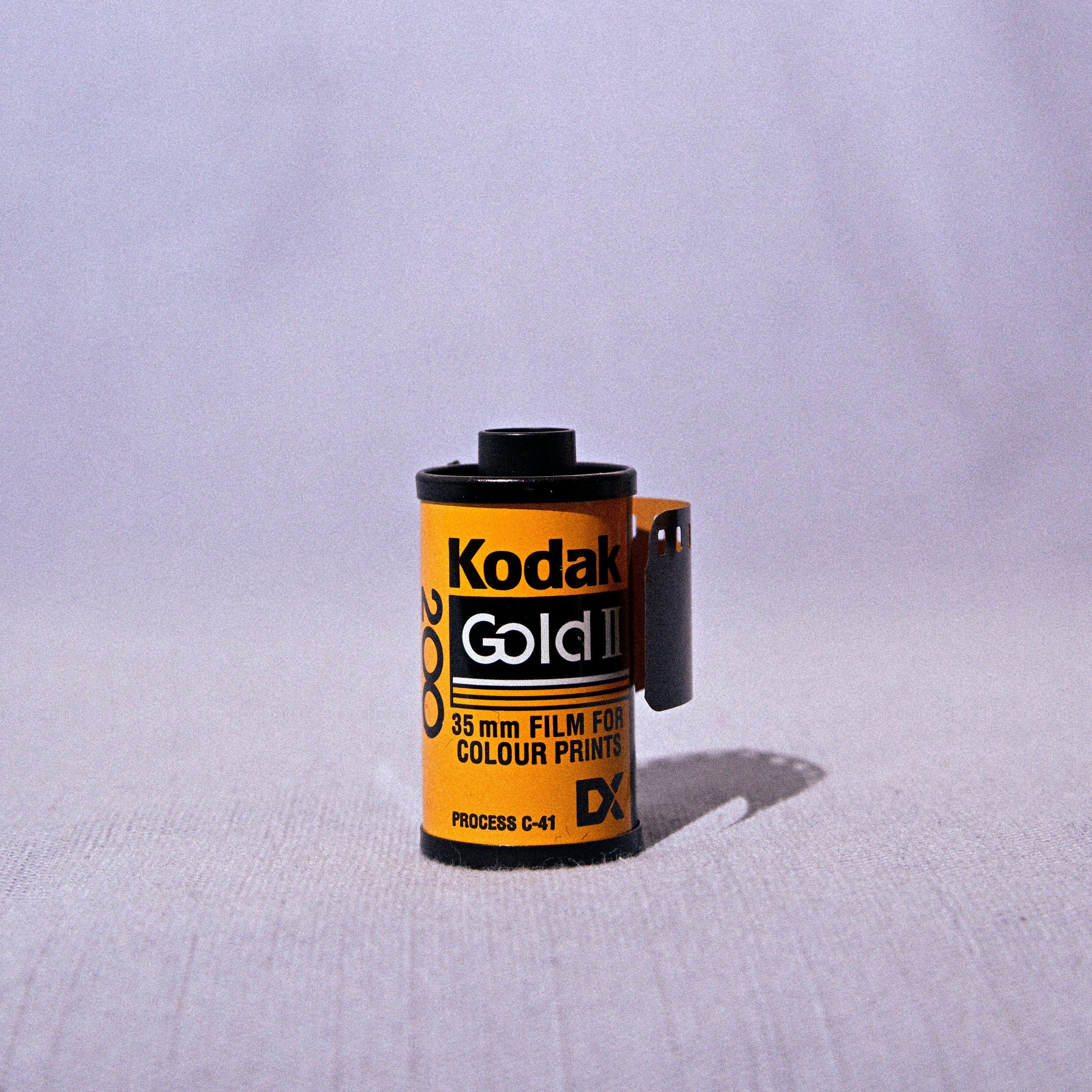 A single roll of vintage Kodak Gold II color film positioned upright on a light gray fabric surface against a matching draped background.