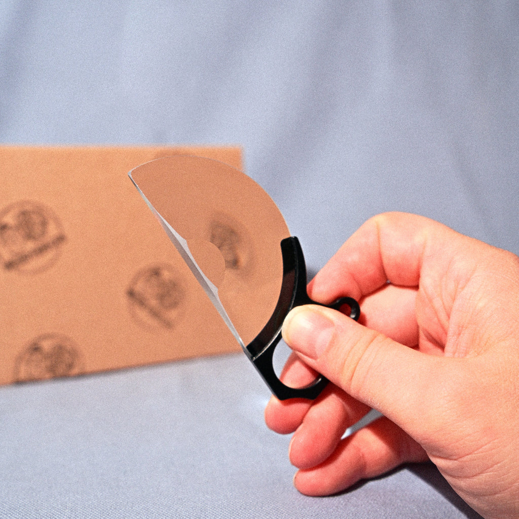 Hand holding a pair of scissors cutting a piece of cardboard on a blue background