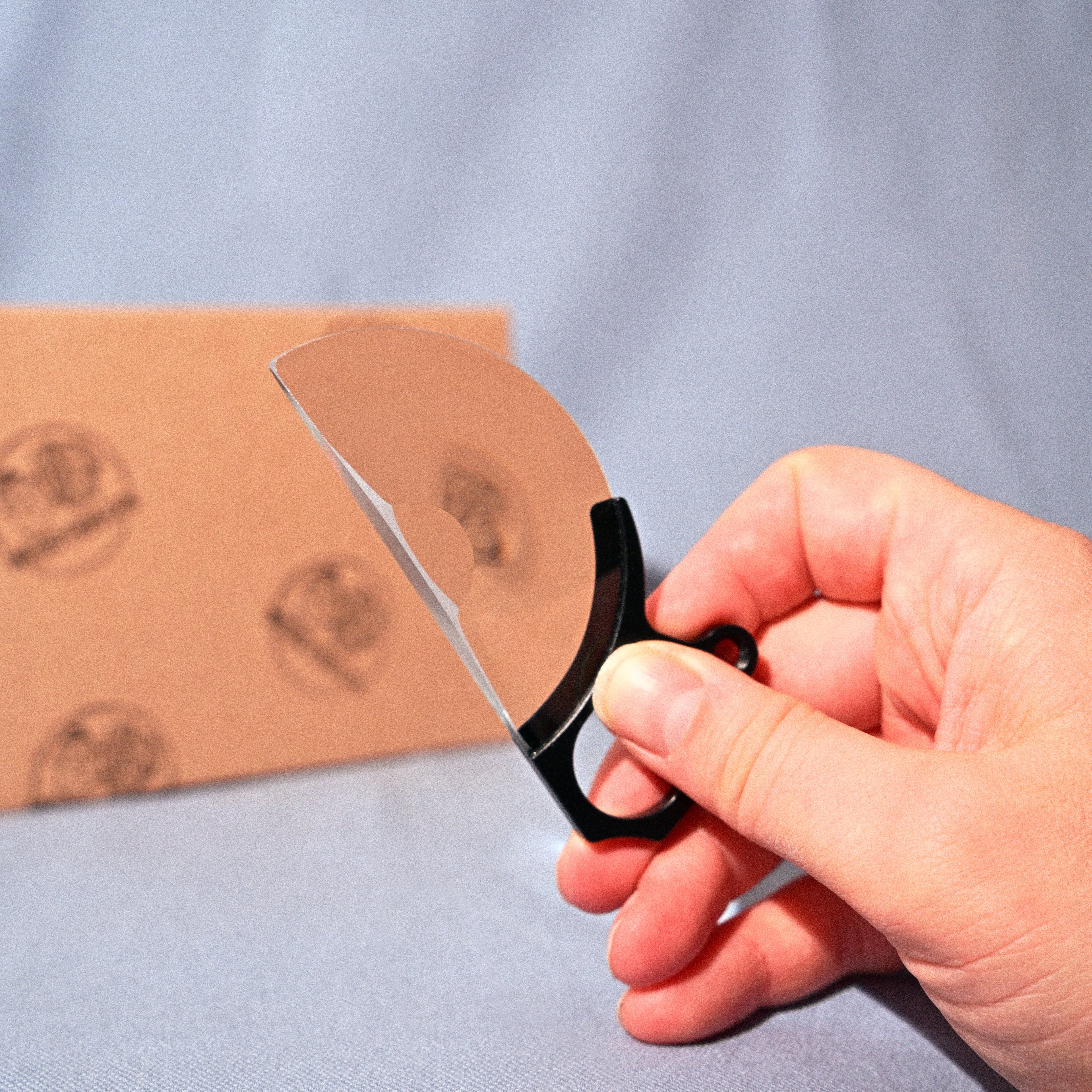 Hand holding a pair of scissors cutting a piece of cardboard on a blue background