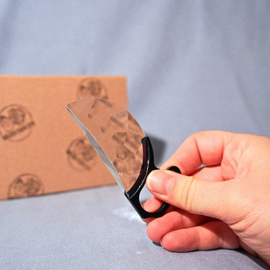 Hand holding a pair of scissors cutting a piece of cardboard on a gray background