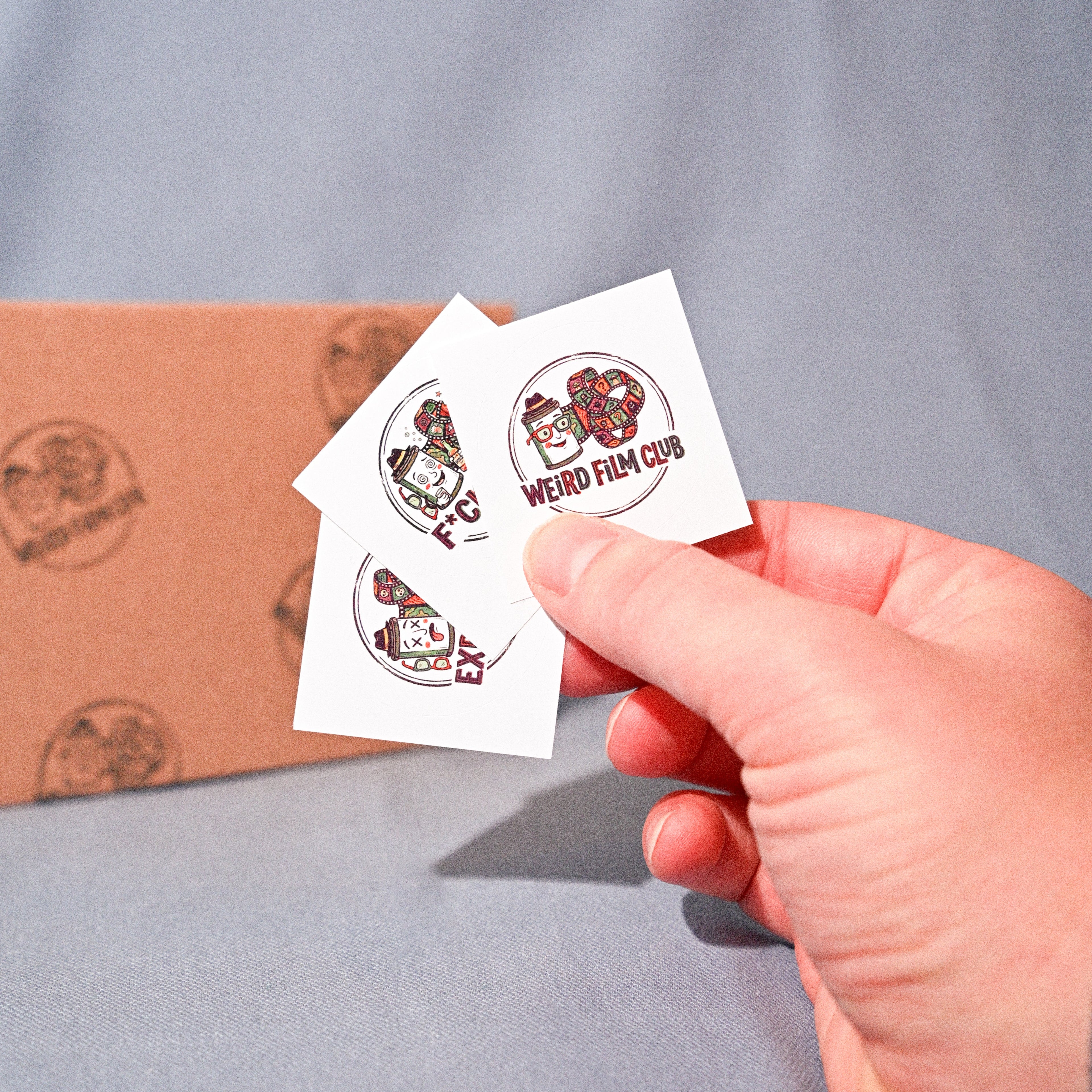 Hand holding three small white stickers with red and black designs against a gray background