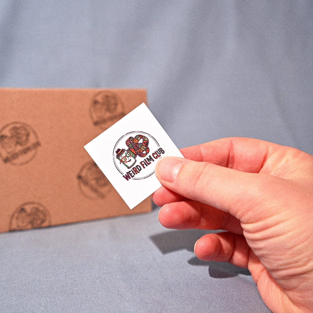 Hand holding a small white card with a logo in front of a cardboard box on a gray background