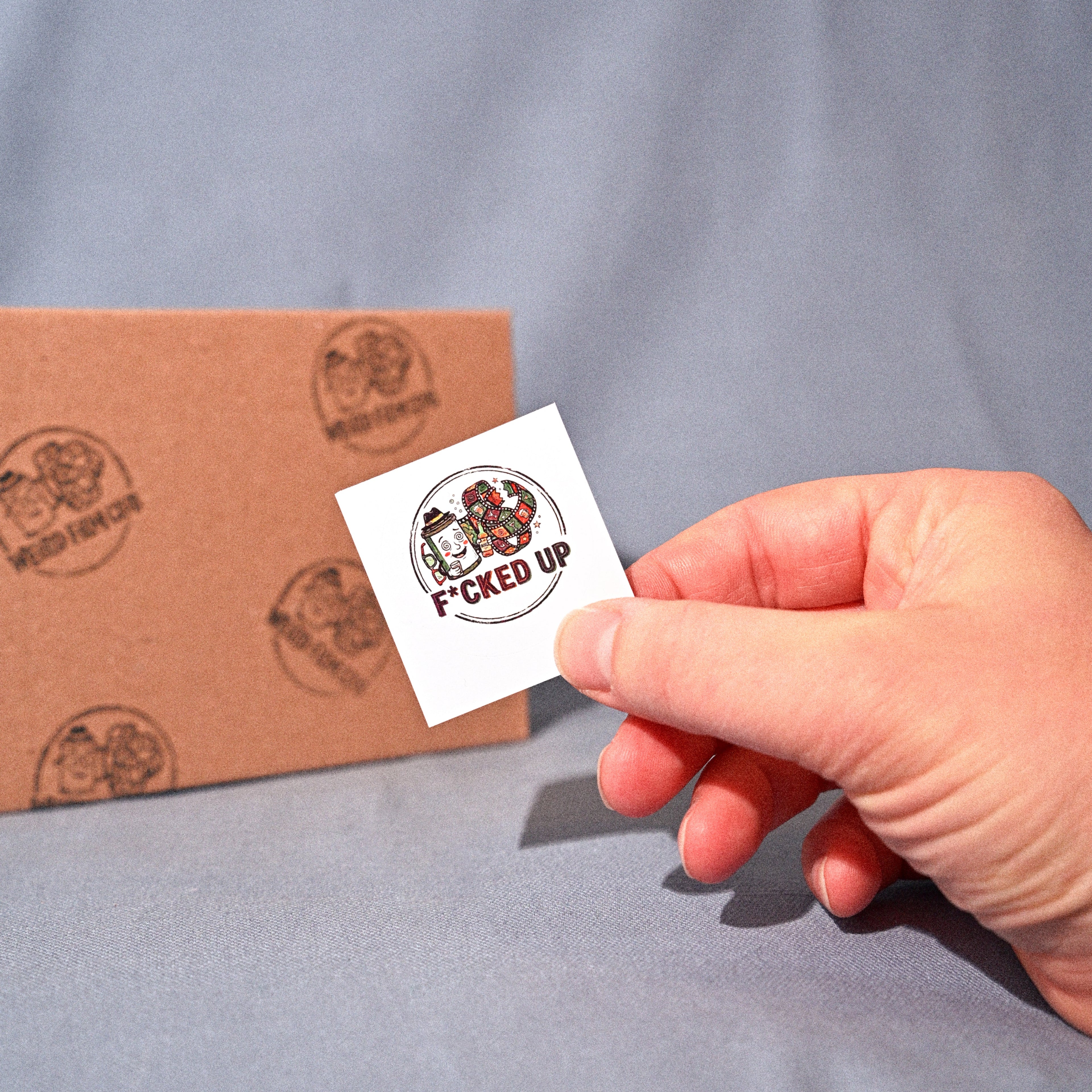 Hand holding a small white card with text next to a cardboard box on a gray background