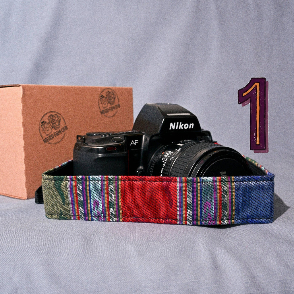 Nikon camera with a colorful strap on a gray surface, with a cardboard box and number '1' in the background.