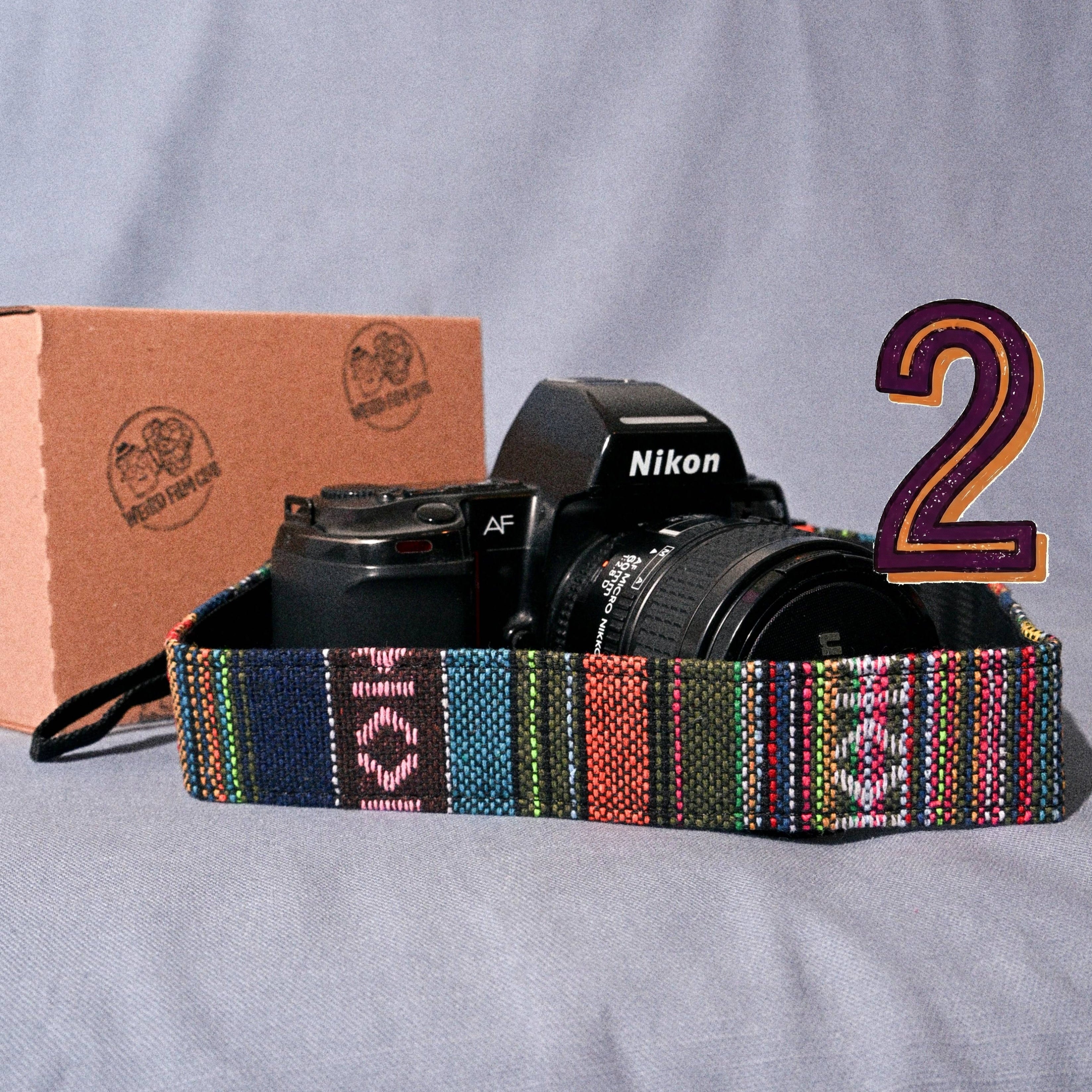 Camera with a colorful strap on a gray surface, with a cardboard box in the background.